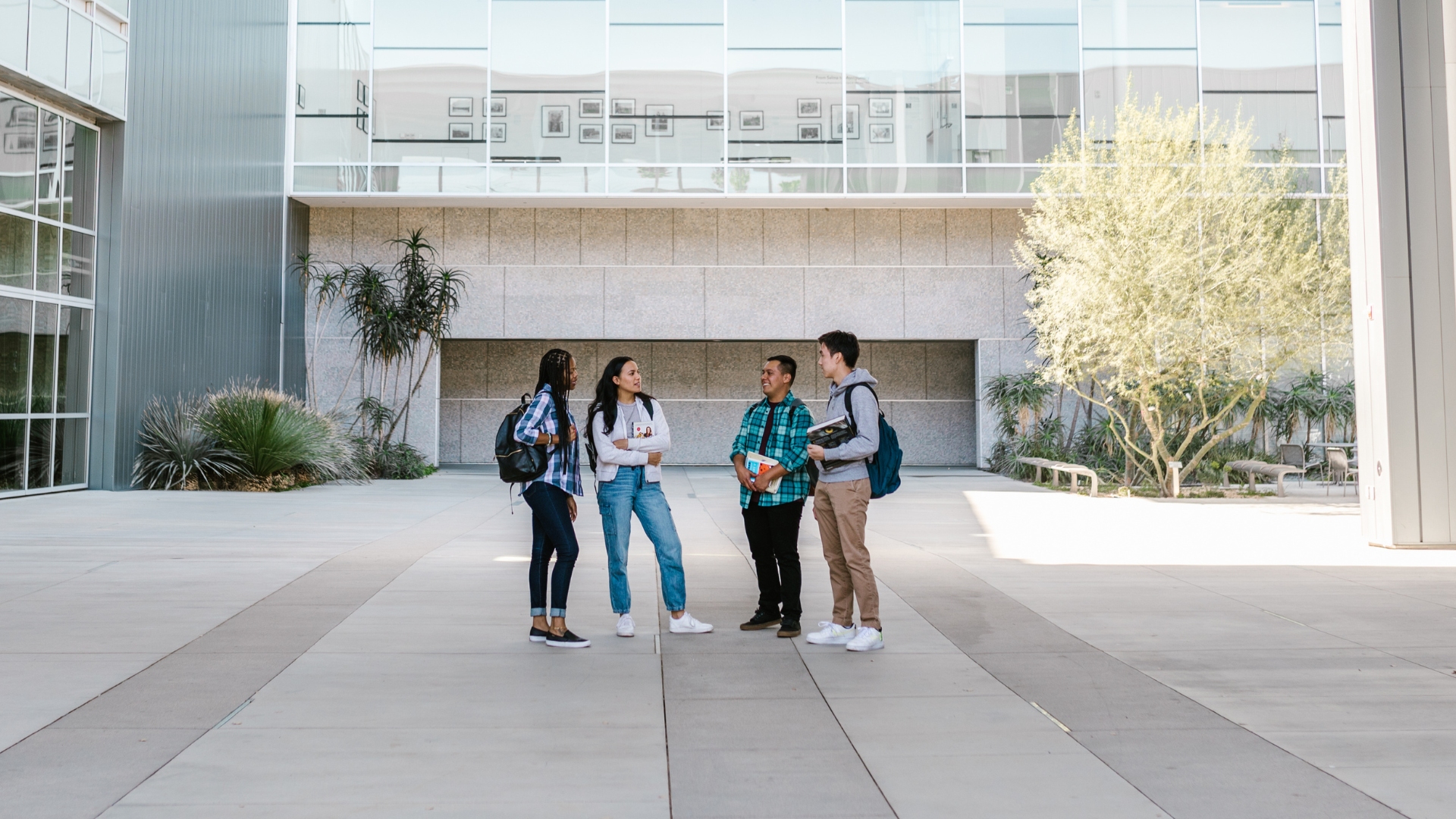Four college students stand talking in front of building